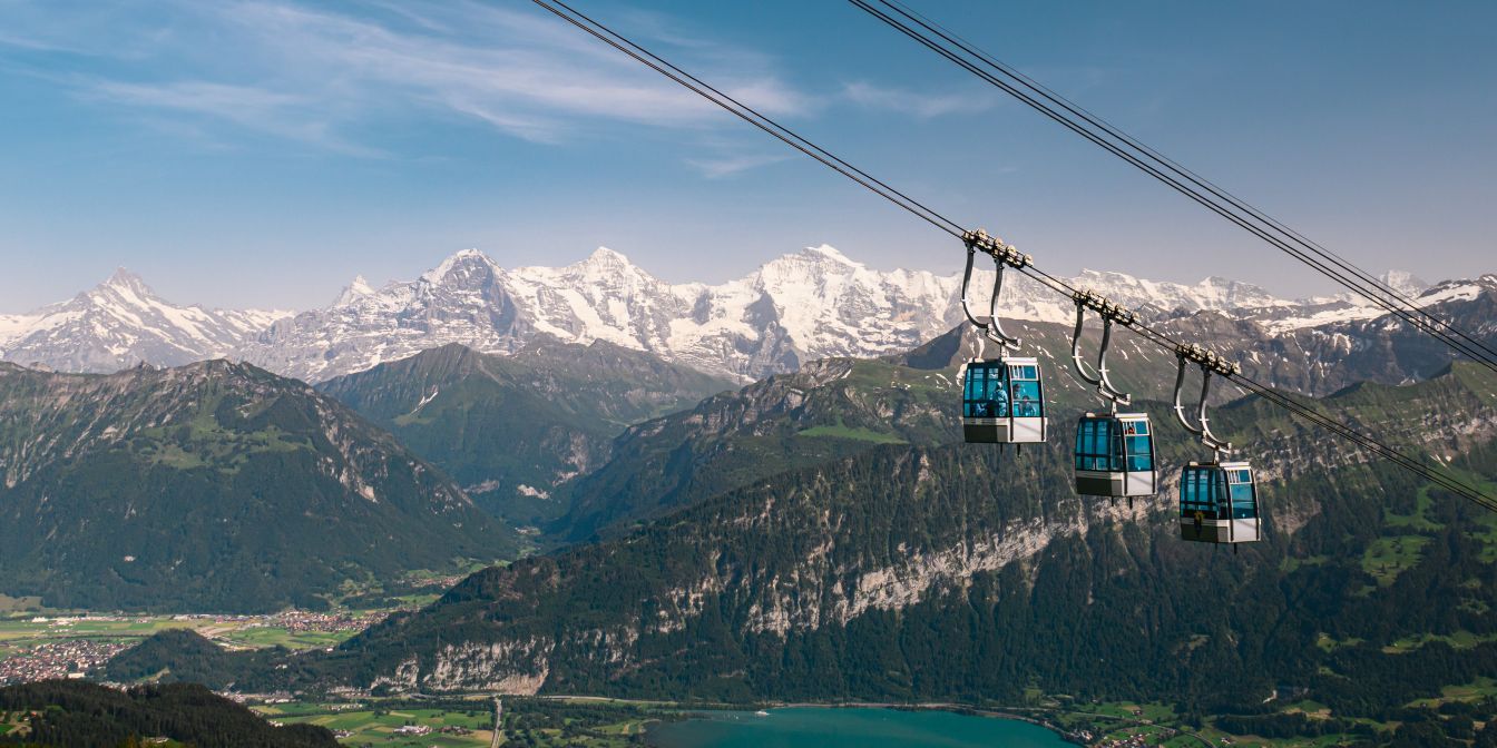 Mehrere Gondeln schweben über dem Tal; im Hintergrund glitzern Thunersee und schneebedeckte Gipfel – inspirierende Kulisse für Events in der Region Thun. ©Niederhorn Seilbahn-Gondeln mit Blick auf den Thunersee und die Berner Alpen