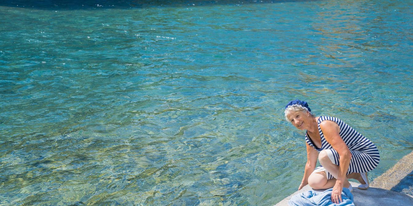 Sommermoment am Thunersee: Eine Frau sitzt am Steg und lässt die Hand ins türkisfarbene Wasser baumeln – entspannt, erfrischend und ideal als leichtes Rahmenprogramm für Meetings, Seminare oder Team-Events in der Region. ©Thun-Thunersee Tourismus Frau am Ufer des Thunersees beim Abkühlen der Füsse im klaren Wasser