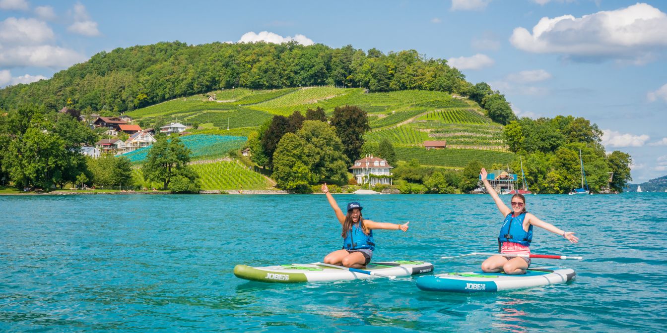 Zwei Personen beim Stand-up-Paddling auf dem Thunersee mit gr&uuml;nen H&uuml;geln im Hintergrund