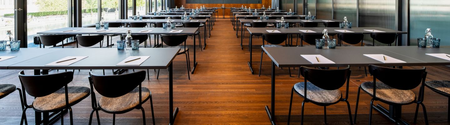 Heller Konferenzraum in Reihenbestuhlung mit Holzboden, moderner Beleuchtung und Blick ins Grüne – ideal für Meetings und Workshops in der Region Thun. ©Hotel Aare Moderner Seminarraum mit Tischreihen und Panoramafenstern am Thunersee
