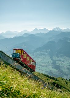 Rote Schmalspurbahn f&auml;hrt am Berghang mit Blick auf die Alpen
