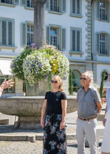 A local guide leads a small group near a flower fountain in Thun, offering an inspiring cultural add-on for corporate events at Lake Thun. ©Thun-Thunersee Tourismus Guided city tour group in Thun Old Town, Switzerland, by historic building