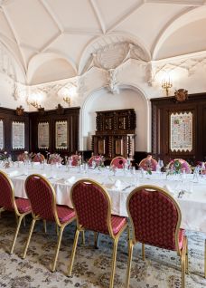Festlich gedeckte Tafel in einem historischen Saal mit Gewölbedecke, Holzvertäfelung und Kronleuchtern – ideal für Meetings und Dinner in Thun. ©Schloss Oberhofen Eleganter Bankettsaal mit langer Tafel und roten Stühlen in historischem Ambiente