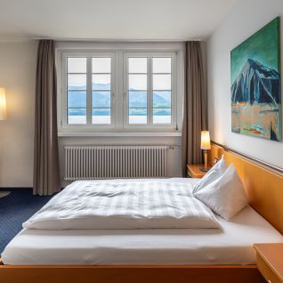 Helles Hotelzimmer mit Doppelbett und Blick auf den Thunersee und die Berge