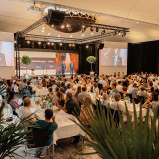 A plenary hall with a keynote speaker and a large audience at a business event in Thun