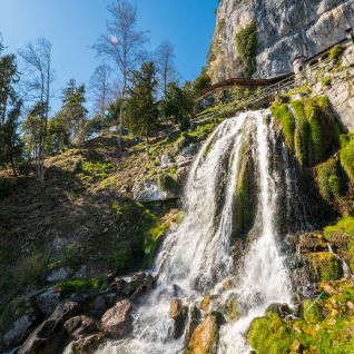 Wasserfall am Felsabhang mit moosigen Steinen und Wald im Berner Oberland