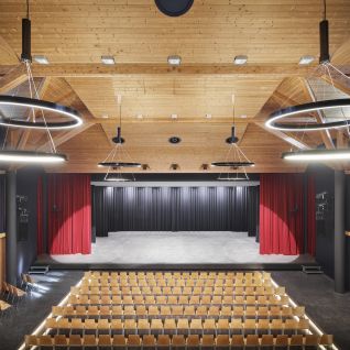 A modern event hall with a stage, tiered seating and ring lights in Thun