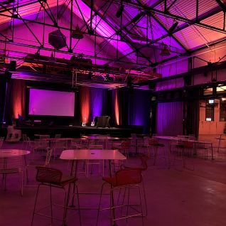 Event hall with a stage and screen, atmospheric purple lighting and seating areas