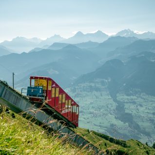Rote Schmalspurbahn fährt am Berghang mit Blick auf die Alpen