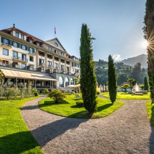 A hotel on Lake Thun with a garden path and a view of the mountains in the evening light
