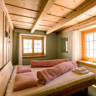 Gemütliches Doppelzimmer mit Holzbalkendecke und karierten Kissen