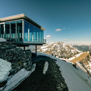 Modernes Panoramarestaurant auf verschneitem Berggrat mit Blick auf die Alpen
