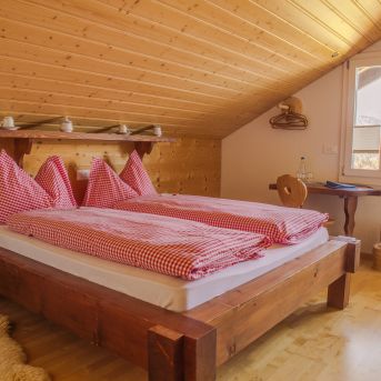 Gemütliches Dachzimmer mit Holzbett und rot kariertem Bettwäsche-Set