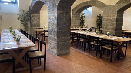 Stimmungsvoller Veranstaltungsraum in Thun mit charakteristischen Steinbögen und langen Holztischen, ideal für Meetings, Workshops oder Firmenfeiern. Warme Beleuchtung und grüne Dekoration schaffen ein einladendes Ambiente für kleine bis mittelgroße B2B-Gruppen in regionalem oder internationalem Kontext. © Schloss Hünegg Historischer Veranstaltungsraum mit Gewölbebögen