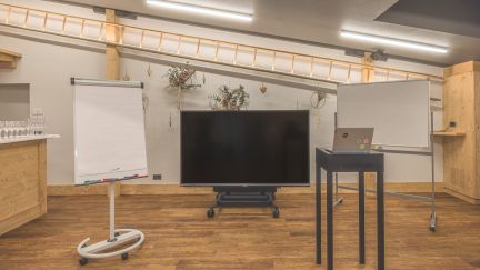 Bright, flexible seminar room with large whiteboards, mobile screen and standing desk on wooden flooring. Ideal for workshops, meetings and training sessions for SMEs, associations and international organisations in the Lake Thun region – with a professional setting for presentations and group work. ©Loube Spiez Modern workshop space on Lake Thun