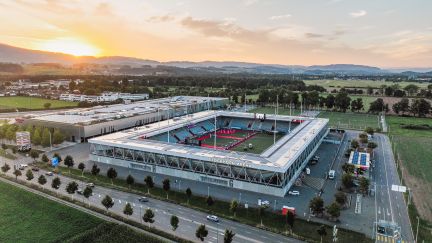 Blick über die Stockhorn Arena in Thun mit Fussballfeld, Alpenpanorama und Abendstimmung – gut erreichbar für Business-Events und Meetings. ©Stockhorn Arena Luftaufnahme der Stockhorn Arena in Thun bei Sonnenuntergang