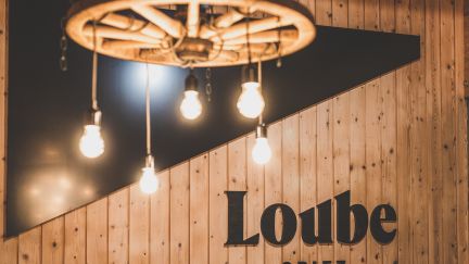 Stimmungsvolle Beleuchtung mit Edison-Glühbirnen vor Holzpaneelen und Loube-Spiez-Logo – ideal für stilvolle Business-Events am Thunersee. ©Loube Spiez Warme Vintage-Lampen und Holzverkleidung im Veranstaltungsraum