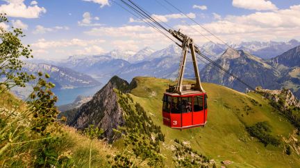 A red cable car gliding over green mountain slopes with a view of Lake Thun