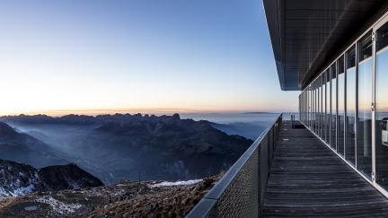 Moderne Holzterrasse entlang einer Glasfront, mit weitem Blick über Gipfel und Nebelmeer – inspirierende Location für Meetings und Events. ©Niesen Panoramaterrasse mit Glasfassade und Blick auf die Berner Alpen bei Sonnenaufgang