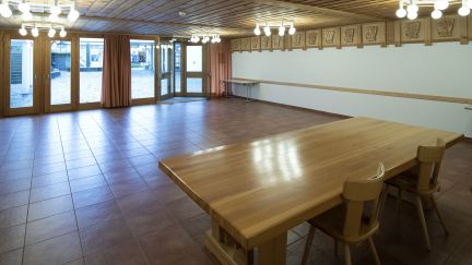 A spacious, light-filled function room with a wooden ceiling, tiled floor and access to the outdoors – ideal for meetings and workshops on Lake Thun. ©Gemeindezentrum Spiez A bright seminar room with a wooden table, chairs and large windows in Spiez