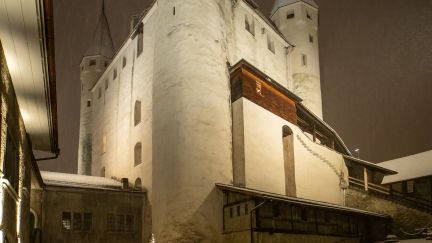 Schnee bedeckt den Innenhof von Schloss Thun; warmes Licht und historische Türme schaffen eine stimmungsvolle Kulisse für Events am Thunersee. @Schloss Thun Schloss Thun im Winter bei Nacht mit verschneitem Innenhof und Lichtern