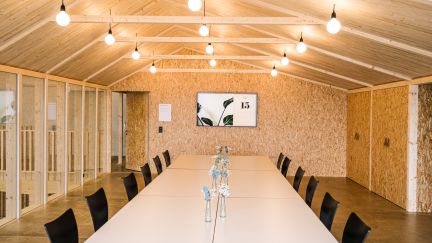 A modern meeting room with a long row of tables, black chairs and a warm wooden interior – ideal for workshops and seminars in the Thun-Thunersee region. ©Westhalle Thun A bright seminar room with a long table and a wooden ceiling on Lake Thun