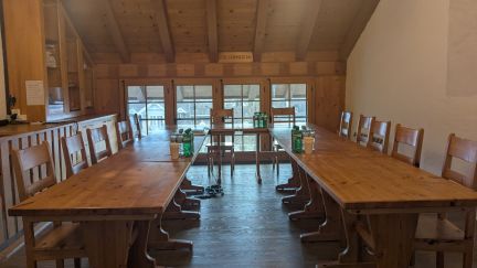 Heller Seminarraum mit Holztischen in U-Form, offener Balkendecke und grosser Fensterfront – ideal für Workshops und Meetings in der Region Thun-Thunersee. ©Schloss Thun Rustikaler Meetingraum mit U-Bestuhlung aus Holz und Blick ins Grüne am Thunersee