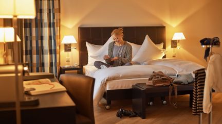 Gemütliches Hotelzimmer mit Doppelbett, Schreibtisch und Leselampen – ideal für Business-Aufenthalte und ruhige Eventvorbereitung in der Region Thunersee. © Hotel Seepark, Thun Geschäftsreisende im Hotelzimmer mit Doppelbett und warmem Licht