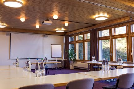 Modern, light-filled seminar room with U-shaped seating, projector and large screen. The window front offers a view of the countryside and creates a peaceful working atmosphere – ideal for workshops, meetings and training courses for SMEs, associations and international organisations in the Lake Thun region. ©Meielisalp Seminar Room on Lake Thun