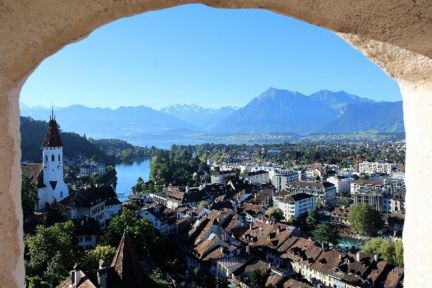 Blick durch einen Torbogen auf Thun, Schlosskirche und den Thunersee mit Alpenpanorama