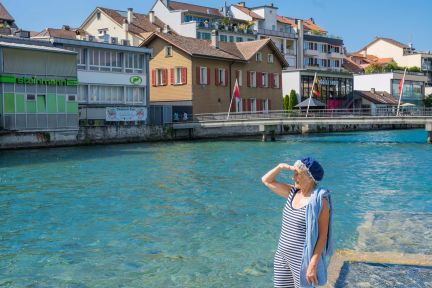 A summer scene by the clear water: a woman strolling along the jetty, with the harbour basin and a row of historic houses in Thun on Lake Thun in the background. Themed guided tours are ideal as a supporting programme after a long day of seminars. ©Thun-Thunersee Tourism A woman on the shore looking out over the harbour and the old town houses in Thun on Lake Thun