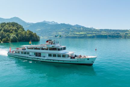 A modern passenger ship glides across the turquoise waters of Lake Thun, with mountain panoramas and a clear summer atmosphere in the background. Ideal for corporate events, meetings or incentives on the lake – an inspiring backdrop in the Lake Thun region, Canton of Bern. Event ship on Lake Thun
