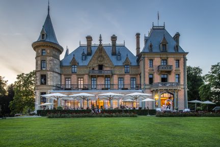 Abendstimmung vor Schloss Schadau am Thunersee: historisches Palais, helle Sonnenschirme und Gäste auf der Terrasse – ideal für exklusive Business-Events. ©Schloss Schadau Schloss Schadau in Thun mit beleuchteter Terrasse und Eventbestuhlung am Abend