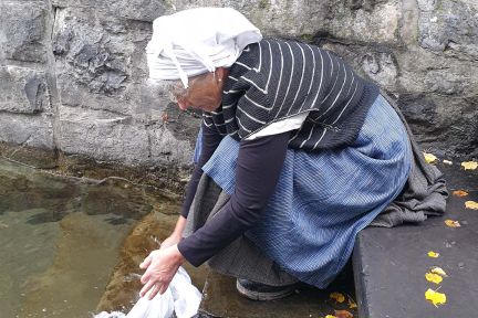 Frau w&auml;scht W&auml;sche am Brunnen vor Natursteinmauer in der Thunersee-Region