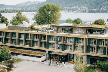 Moderne Hotelanlage mit Holzfassade und grosszügigen Balkonen, eingebettet ins Grün direkt am Thunersee. Im Hintergrund liegen See und Alpenpanorama. Ideal für Seminare, Meetings und Firmenanlässe in der Region Bern – mit ruhiger Lage, inspirierender Aussicht und professioneller Infrastruktur. ©Deltapark Deltapark Vitalresort am Thunersee