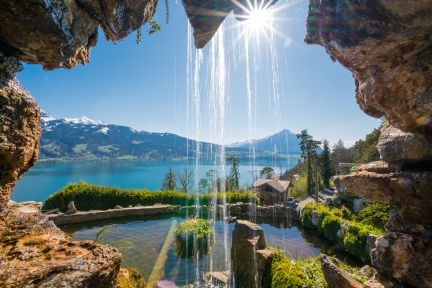 Blick durch eine Grotte auf den Thunersee mit Wasserfall und Alpenpanorama