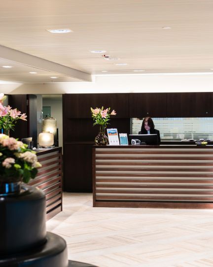 Helle, moderne Lobby mit elegantem Empfangsbereich in Thun. Frische Blumenarrangements setzen stilvolle Akzente, während die freundliche Rezeption einen professionellen Service für Tagungsgäste bietet. Perfekte Location für Geschäftsanlässe und Firmenevents am Thunersee – optimal für nationale und internationale Unternehmen. © Hotel Seepark, Thun Einladende Hotellobby mit Rezeption