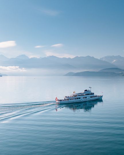 Ein Schiff zieht ruhige Wellen über den Thunersee; im Hintergrund liegen Berge und Nebel – inspirierende Kulisse für Business-Events in der Region. ©BLS Schifffahrt AG Passagierschiff auf dem Thunersee vor Alpenpanorama am Morgen