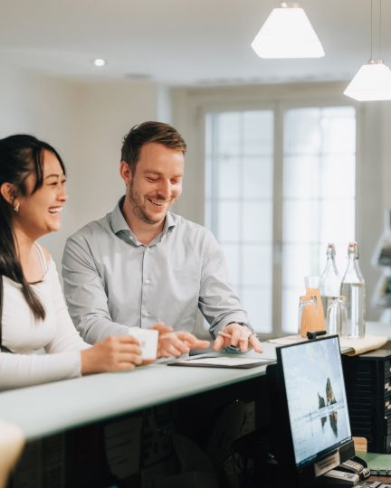Freundlicher Empfang am Front Desk: Zwei Gäste besprechen Unterlagen mit der Gastgeberin – ideal für Meetings und Business-Events am Thunersee. ©Hotel Krone Business-Gäste beim Check-in an einer Hotelrezeption im Thunersee-Meeting-Setting