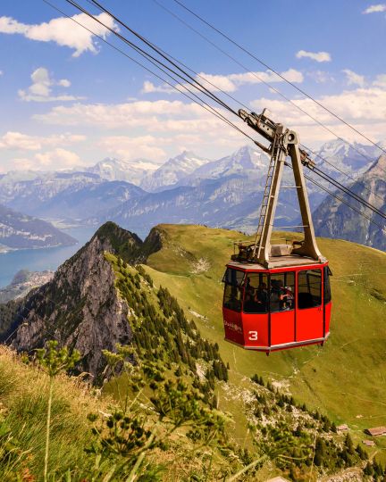 Die Stockhornbahn schwebt majestätisch über die grünen Alpenhänge, mit eindrucksvollem Blick auf den Thunersee und das Berner Oberland. Das sonnige Sommerwetter und die imposante Bergkulisse schaffen ein inspirierendes Ambiente – ideal für Firmenveranstaltungen und Teamevents in der Region Thunersee. @Stockhorn Moderne Stockhornbahn mit Panoramablick
