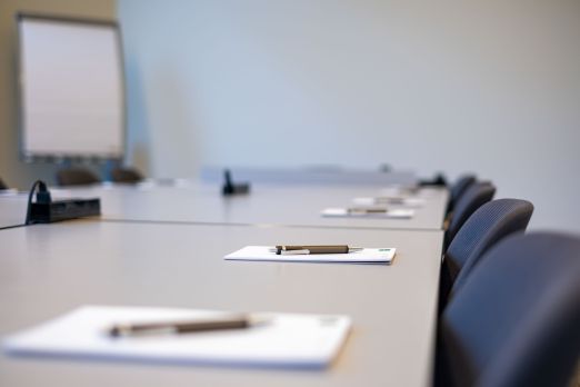 Ein heller, moderner Gruppenraum mit einer langen Tischreihe, bestückt mit Stühlen und vorbereitet mit Schreibblöcken und Stiften. Im Hintergrund steht ein Flipchart bereit – ideal für Workshops, Seminare und Besprechungen am Thunersee. Perfekte Voraussetzungen für produktive Geschäftsevents. Moderne Gruppenräume für Meetings