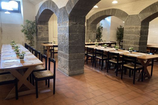 Stimmungsvoller Veranstaltungsraum in Thun mit charakteristischen Steinbögen und langen Holztischen, ideal für Meetings, Workshops oder Firmenfeiern. Warme Beleuchtung und grüne Dekoration schaffen ein einladendes Ambiente für kleine bis mittelgroße B2B-Gruppen in regionalem oder internationalem Kontext. © Schloss Hünegg Historischer Veranstaltungsraum mit Gewölbebögen