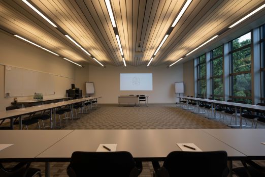 Heller, großzügiger Konferenzraum mit moderner Beleuchtung und bodentiefen Fenstern. Die Tische sind U-förmig für Gruppenarbeiten und Präsentationen angeordnet. Blick ins Grüne sorgt für inspirierende Atmosphäre – ideal für Workshops, Meetings und Tagungen in Thun und Umgebung. London - Moderner Konferenzraum mit Blick ins Grüne