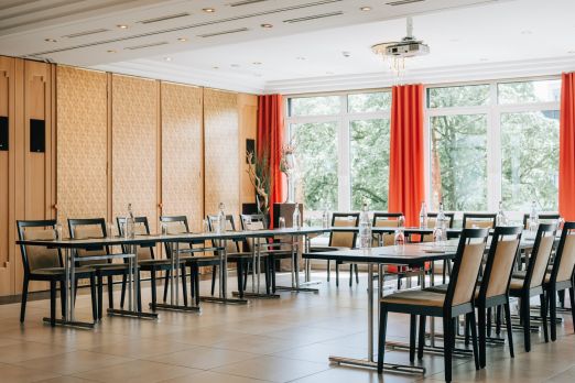 Heller Meetingraum im Thunersee-Region: U-Bestuhlung mit Tischen, viel Tageslicht und ruhige Atmosphäre – ideal für Workshops und Seminare. ©Hotel Krone Seminarraum mit U-Bestuhlung, grossen Fenstern und roten Vorhängen