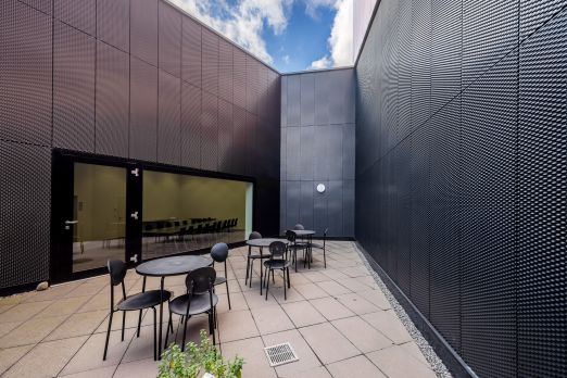 Heller Innenhof mit Tischen und Stühlen zwischen modernen Fassaden – ideal für Kaffeepausen, Breakouts oder Apéros bei Meetings in der Region Thun-Thunersee. ©KKThun Moderner Innenhof mit Sitzgruppen und Terrassentischen für Business-Events