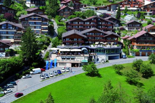 Luftaufnahme eines modernen Veranstaltungsortes inmitten traditioneller Schweizer Chalets oberhalb des Thunersees. Die großzügige Terrasse und der Blick ins Grüne bieten ideale Bedingungen für Business-Events und Tagungen in inspirierender Alpenkulisse. Perfekt für Meetings kleiner und mittlerer Unternehmen. ©Solbad Vogelperspektive auf Veranstaltungsort am Thunersee