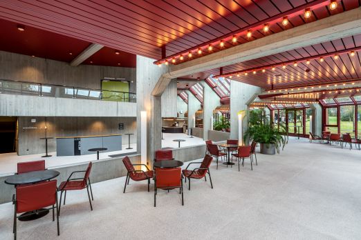 Helle Hotellobby mit roten Sesseln, Glasfront und Blick ins Grüne – ein einladender Treffpunkt für Business-Events in der Region Thun-Thunersee. ©KKThun Moderne Lobby mit Sitzgruppen und Panoramafenstern im Tagungshotel am Thunersee