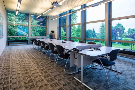 Heller, moderner Seminarraum mit grossen Fensterfronten, Blick ins Grüne und flexibler Tischanordnung für Meetings, Workshops oder Schulungen. Ergonomische Stühle, integrierte Präsentationstechnik und klare Linien schaffen eine professionelle Atmosphäre – ideal für Business-Events am Thunersee im Kanton Bern. ©Seepark Moderner Seminarraum mit Tageslicht