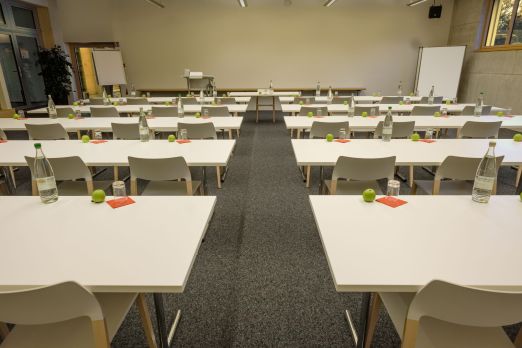 Seminarraum in U-Bestuhlung mit Tischen, Wasserflaschen und Schreibmaterial