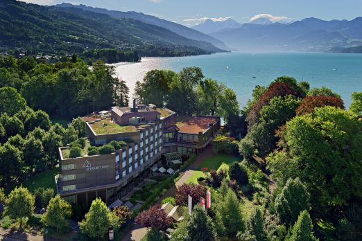 Luftaufnahme eines Seminarhotels am Ufer des Thunersees, umgeben von Wald und Gärten – ruhige Lage mit Blick auf See und Berge. ©Seepark Panoramablick auf ein Seminarhotel am Thunersee mit Alpenkulisse
